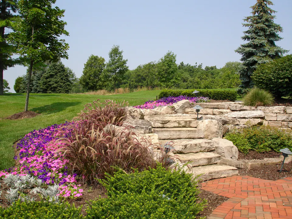 Stone steps and terraced planting with seasonal color, ornamental grasses, shrubs, and a brick walk